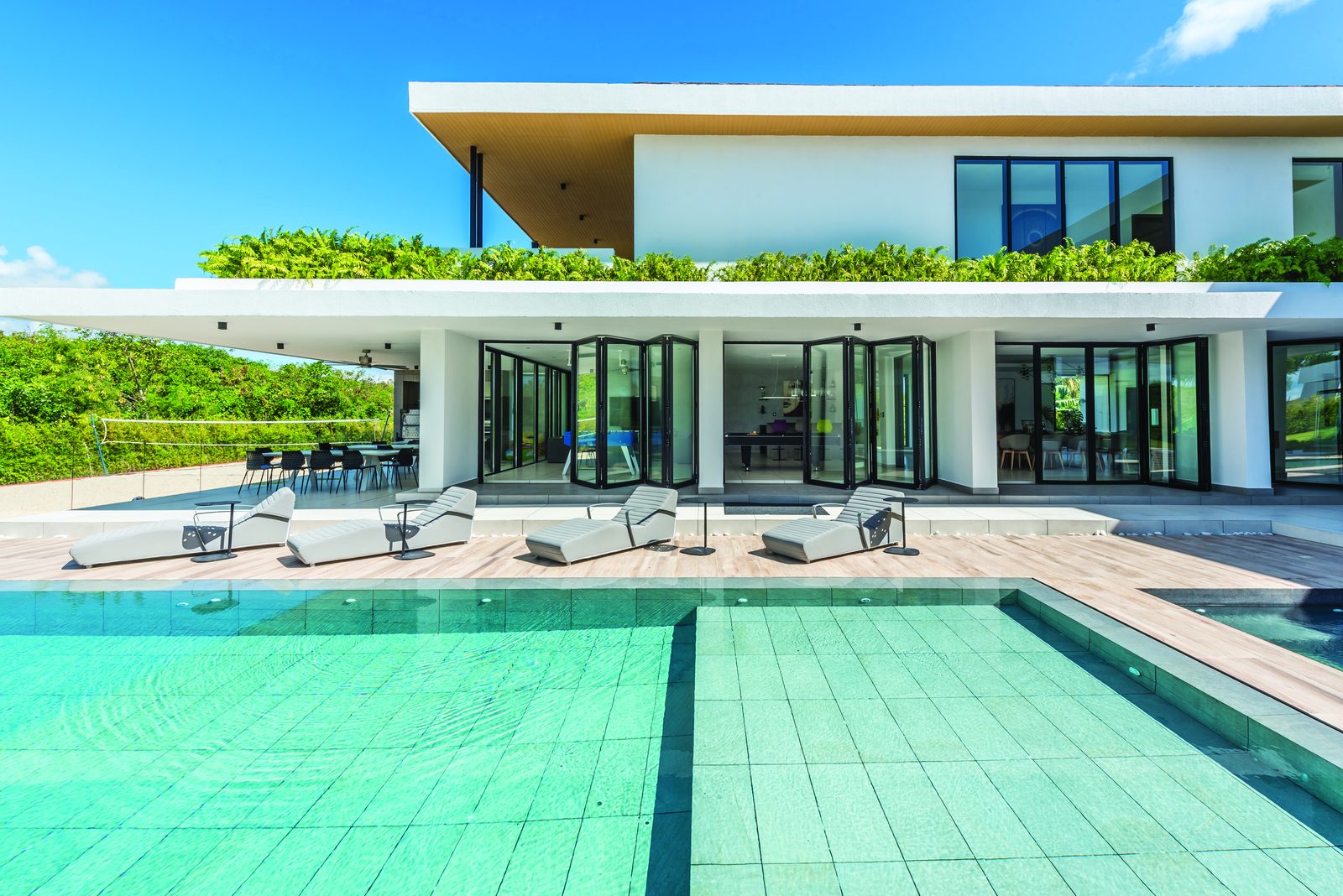 Black aluminium bifold doors across the ground floor of a modern villa beside a pool
