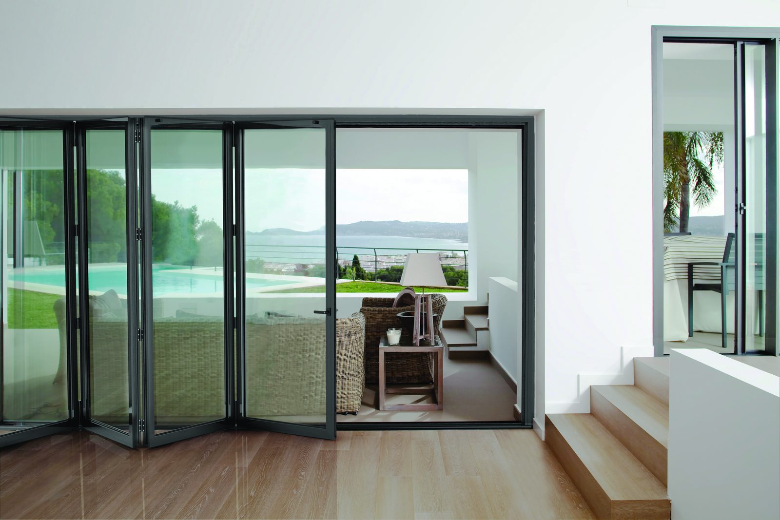 Living room with dark aluminium bifold doors opening onto a pool terrace