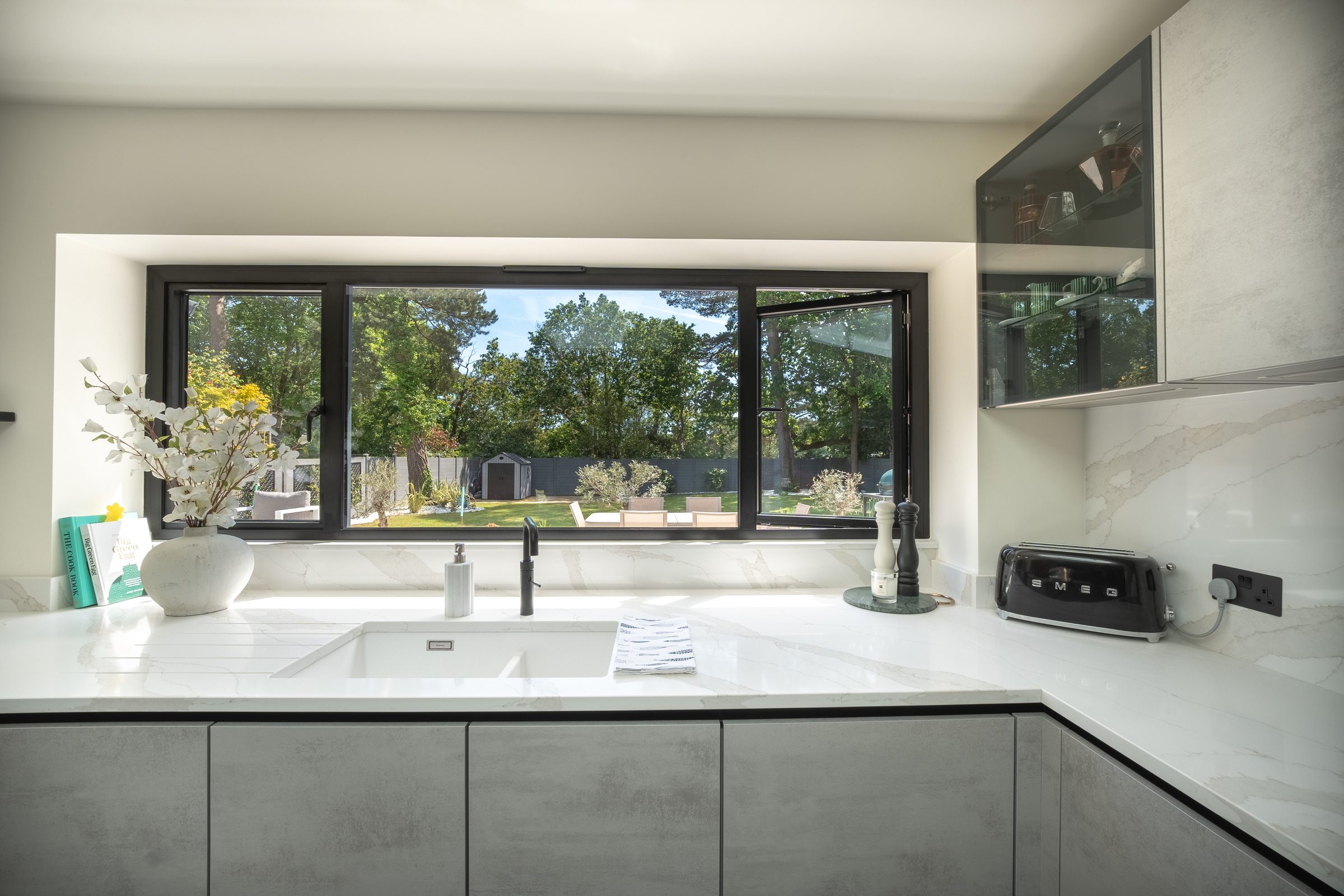 Wide black aluminium casement window over a kitchen sink, looking out to a garden
